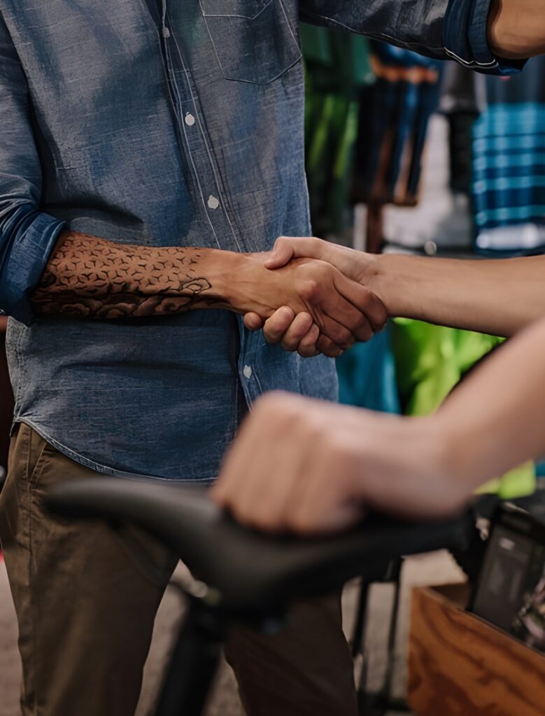 Poignée de main, tatouage tribal et vélo en magasin Gros plan sur une poignée de main entre un homme à la chemise en jean et tatouage tribal et une personne tenant une selle de vélo.