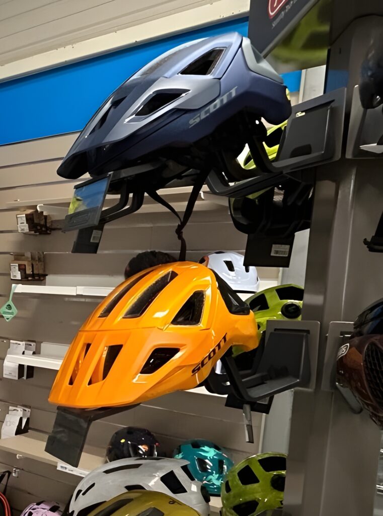 Casques VTT Scott en Magasin : Modèles et Couleurs Casques de vélo Scott exposés, un bleu marine et gris en haut, un orange vif au milieu, avec d'autres couleurs dessous.