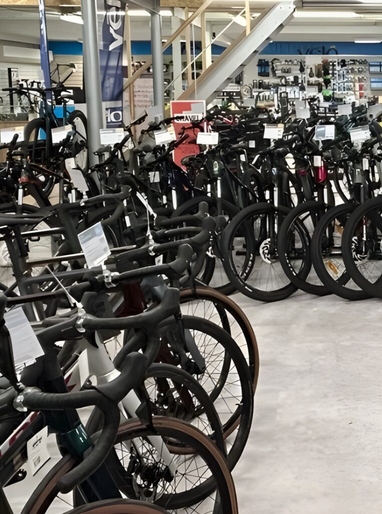 Magasin vélos route et gravel : exposition de modèles noirs Rangs de vélos de route et gravel noirs et blancs avec guidons serrés dans un magasin, affichant des étiquettes et des poteaux avec le mot 'VELO' visible.